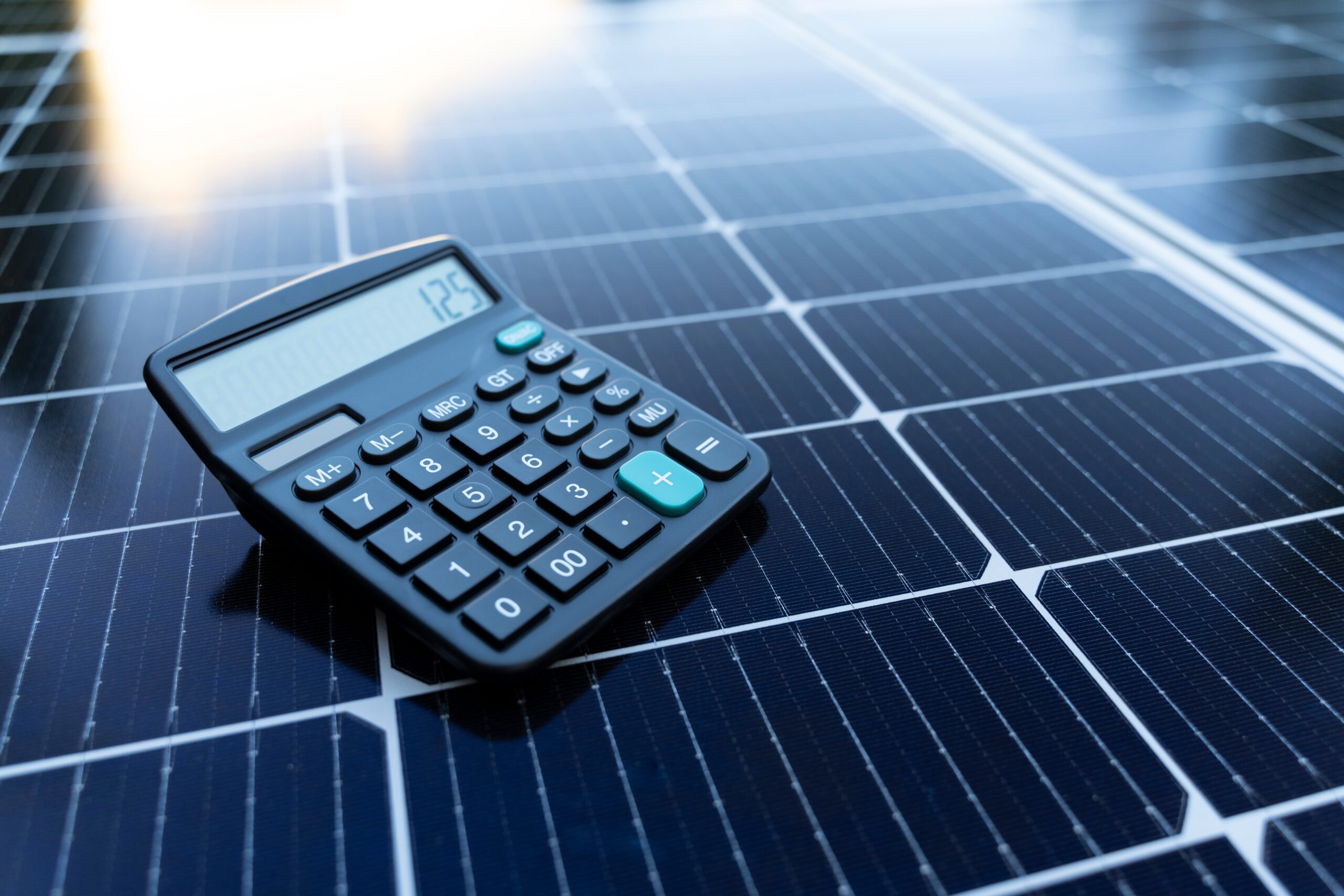 A black calculator displaying the number 125 rests on top of a solar panel under sunlight.